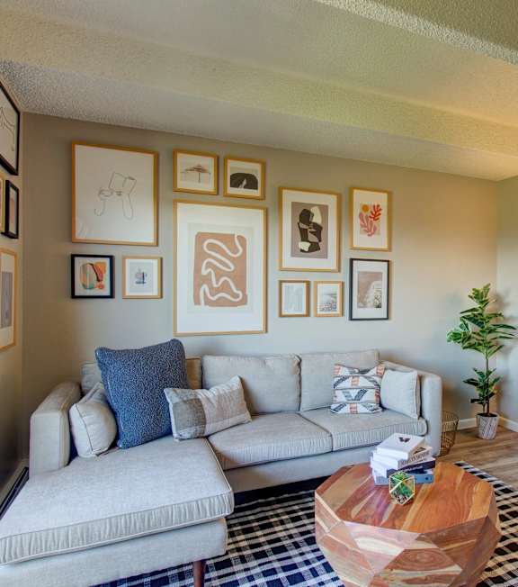 A living room with a grey couch, a wooden chair, a coffee table, and pictures on the wall.