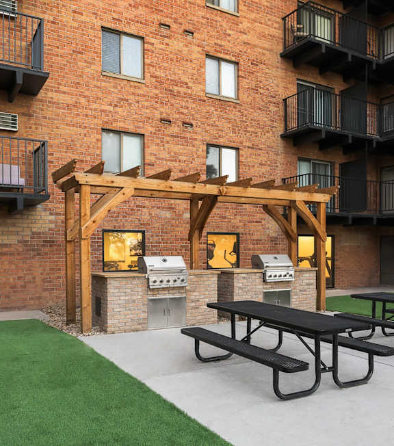 A patio with a picnic table and a grill in front of a brick building.