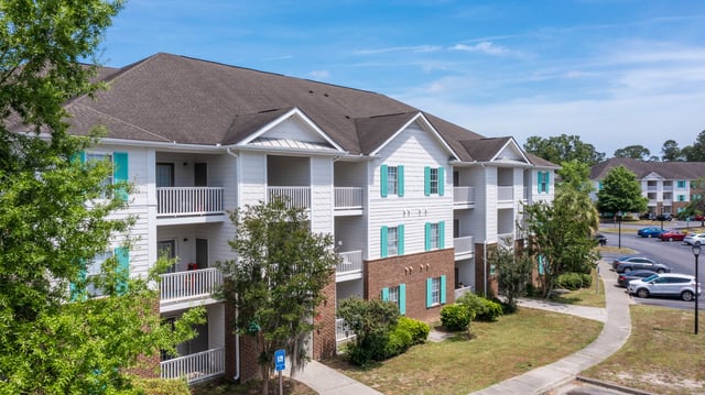 Exterior view of a multi-story apartment building with white siding and teal shutters, featuring bal…