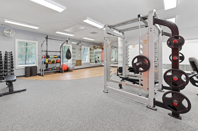 Gym equipment including weight racks, dumbbells, kettlebells, medicine balls, and a punching bag.