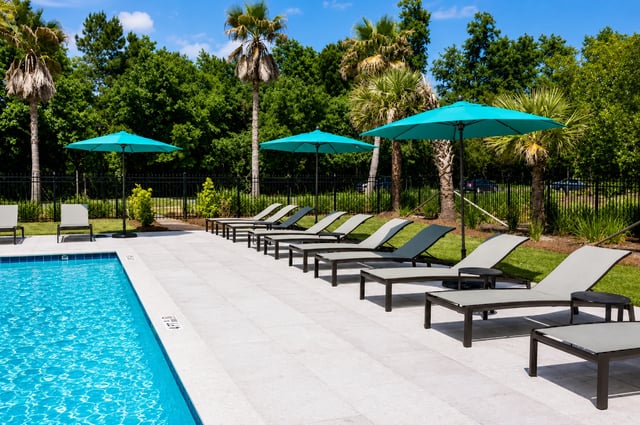 Poolside lounge chairs and umbrellas with palm trees and lush greenery.