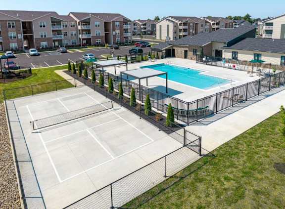 A tennis court is surrounded by a fence and a swimming pool is in the background.
