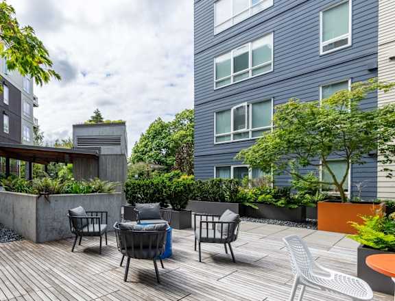 A patio with a table and chairs is surrounded by buildings and trees. at Kirkland Crossing Apartments, Kirkland, WA