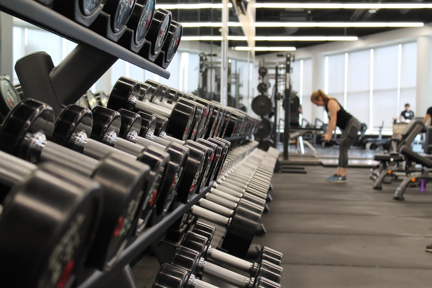 Modern gym interior featuring a variety of dumbbells and weightlifting equipment, with people engaged in workouts.
