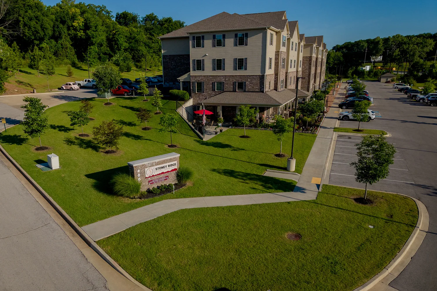 Aerial view of a apartment with landscaped grounds, parking, and a welcoming entrance sign.