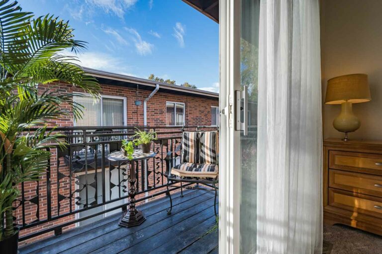 Courtland Ridge Apartments balcony with bistro table, striped chair, and potted plants.
