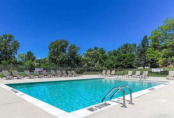 Outdoor swimming pool, surrounded by lounge chairs and landscaping, under a bright blue sky.