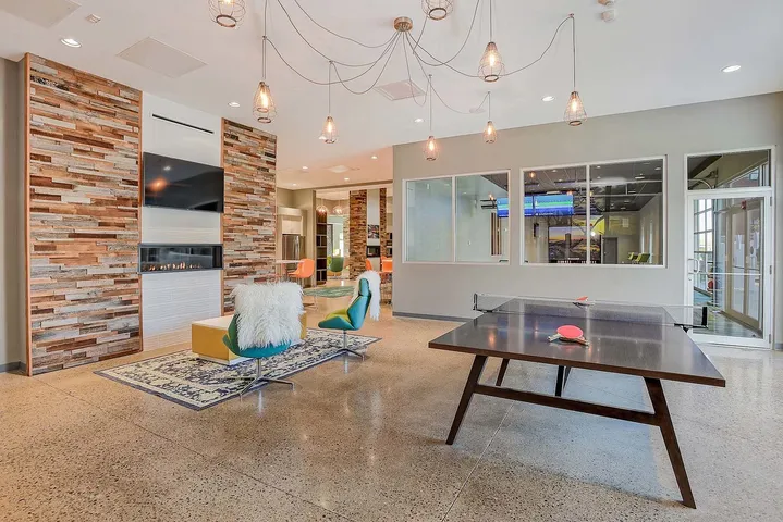 Modern communal space featuring a stylish lounge area with sleek fireplace, vibrant seating, and chic lighting fixtures alongside a ping pong table for recreation.