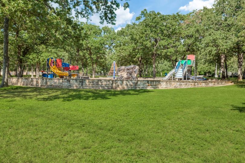 An outdoor playground surrounded by green grass and lush trees.