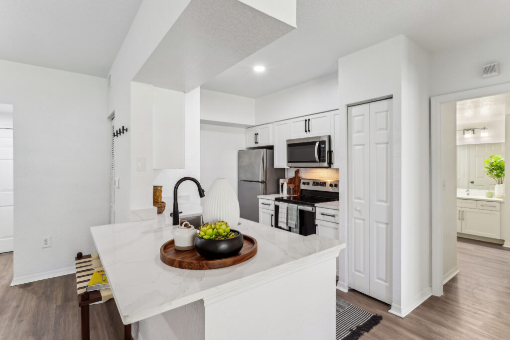 Kitchen with island sink, appliances, wood-style flooring, and designer lighting