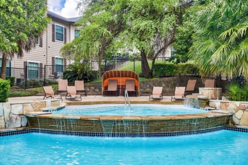 Mission oaks pool with waterfall surrounded by trees and beach chairs and club house