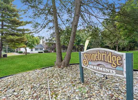 a sign for stonebridge apartments in front of a lawn and trees at Stonebridge, Ellington, CT