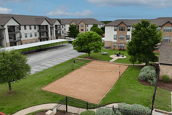A tennis court is surrounded by apartment buildings.