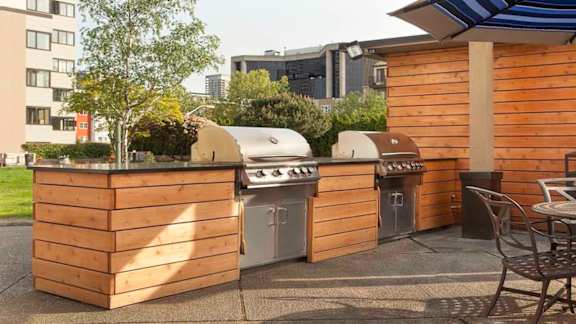 Resident outdoor grilling station with two stainless steel grills and wood paneling at Skye Apartments, Seattle, Washington