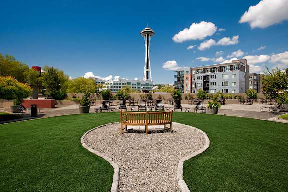 Rooftop green space with a bench and a gravel pathway in the foreground and the Seattle Space Needle in the background at Skye Apartments, Seattle, WA