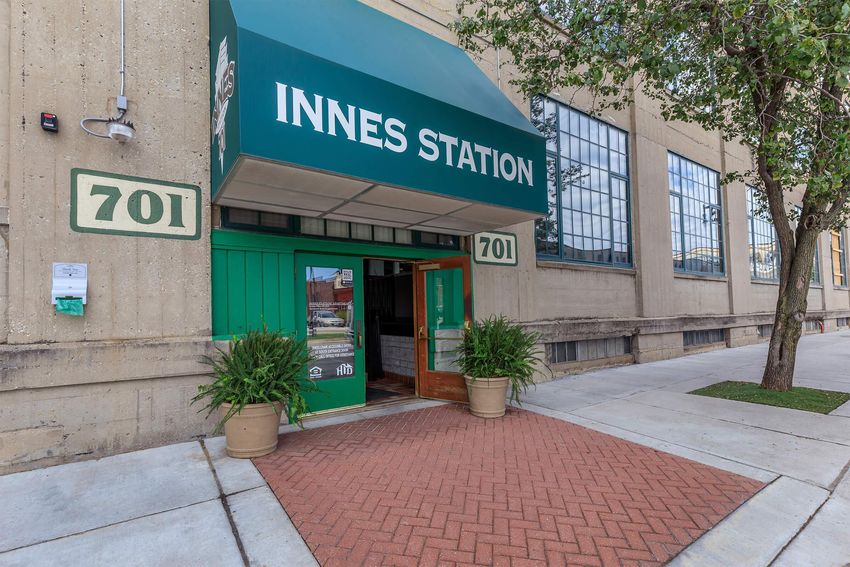 Entrance to Innes Station featuring a green awning with the name "INNES STATION" prominently displayed. The building has large windows and a brick pathway leading to the door, framed by potted plants. The location is marked with the number "701" on the entrance.