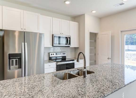North Charleston, SC Townhomes Near The Citadel - Highland Townhomes - Kitchen With Stainless Steel Appliances, White Cabinets, White Tile Backsplash, White Walls, and Granite Countertops
