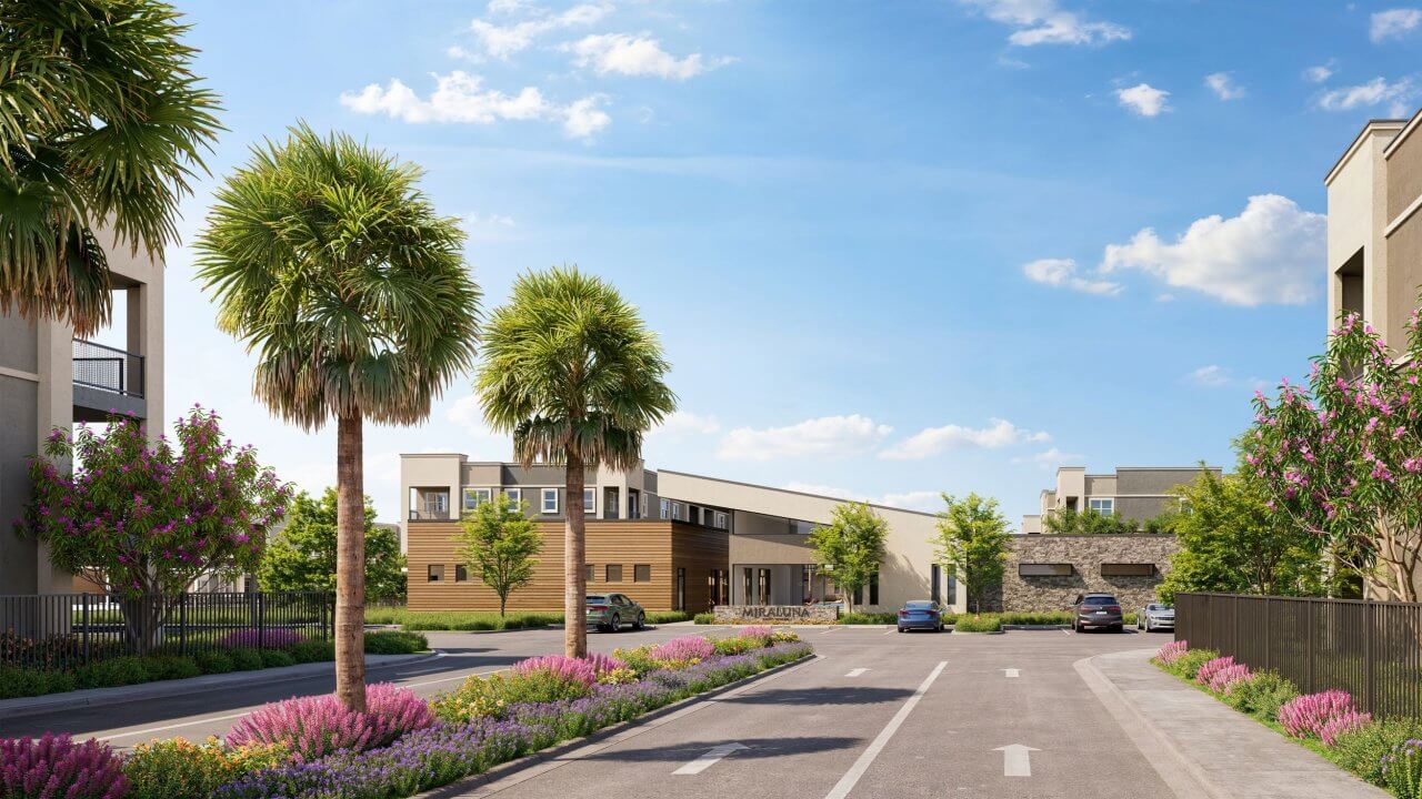Palm-lined entrance and landscaped driveway at Mira Luna apartments in Southwest Las Vegas under a clear blue sky.