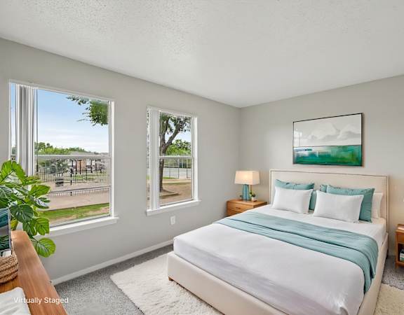 A bedroom with a large bed and a view of a park outside the window.
