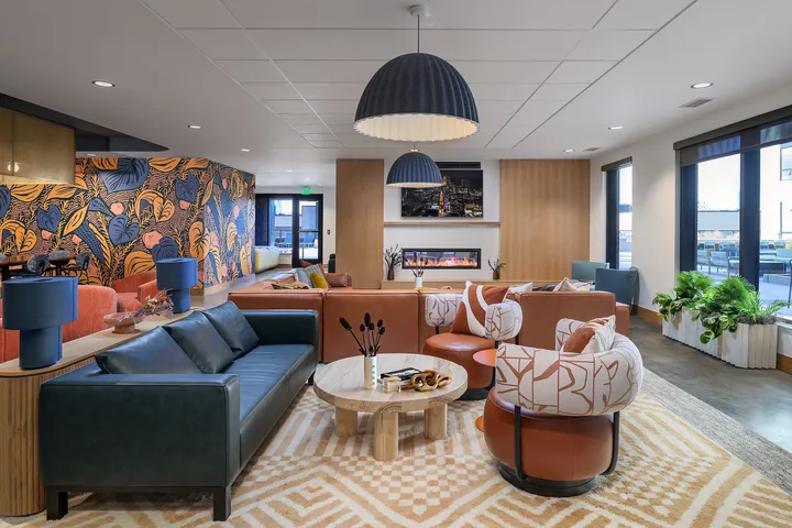 Chic and vibrant living area with stylish furniture, eye-catching wall art, and a cozy fireplace, all illuminated by large windows and modern lighting.