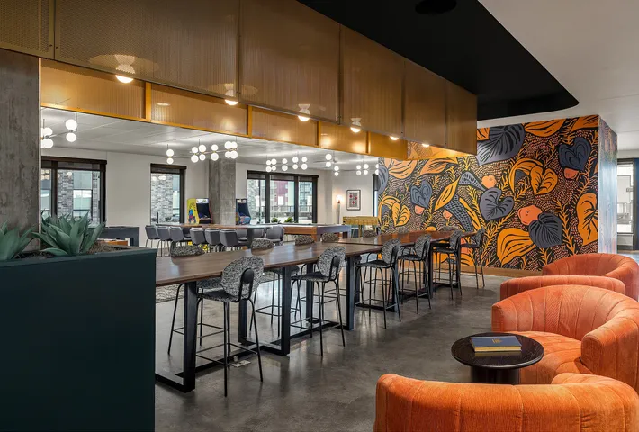 Chic and vibrant communal space boasting modern seating, colorful mural, and ample natural lighting.