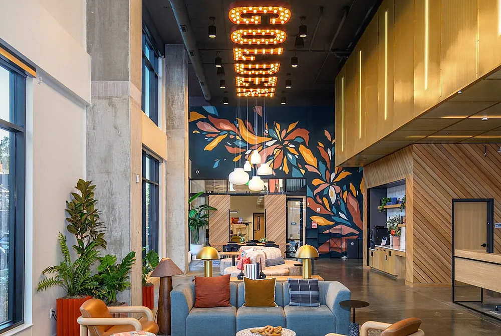 Vibrant lobby with stylish seating, colorful mural, and lit signage, creating a welcoming atmosphere in a modern apartment complex.