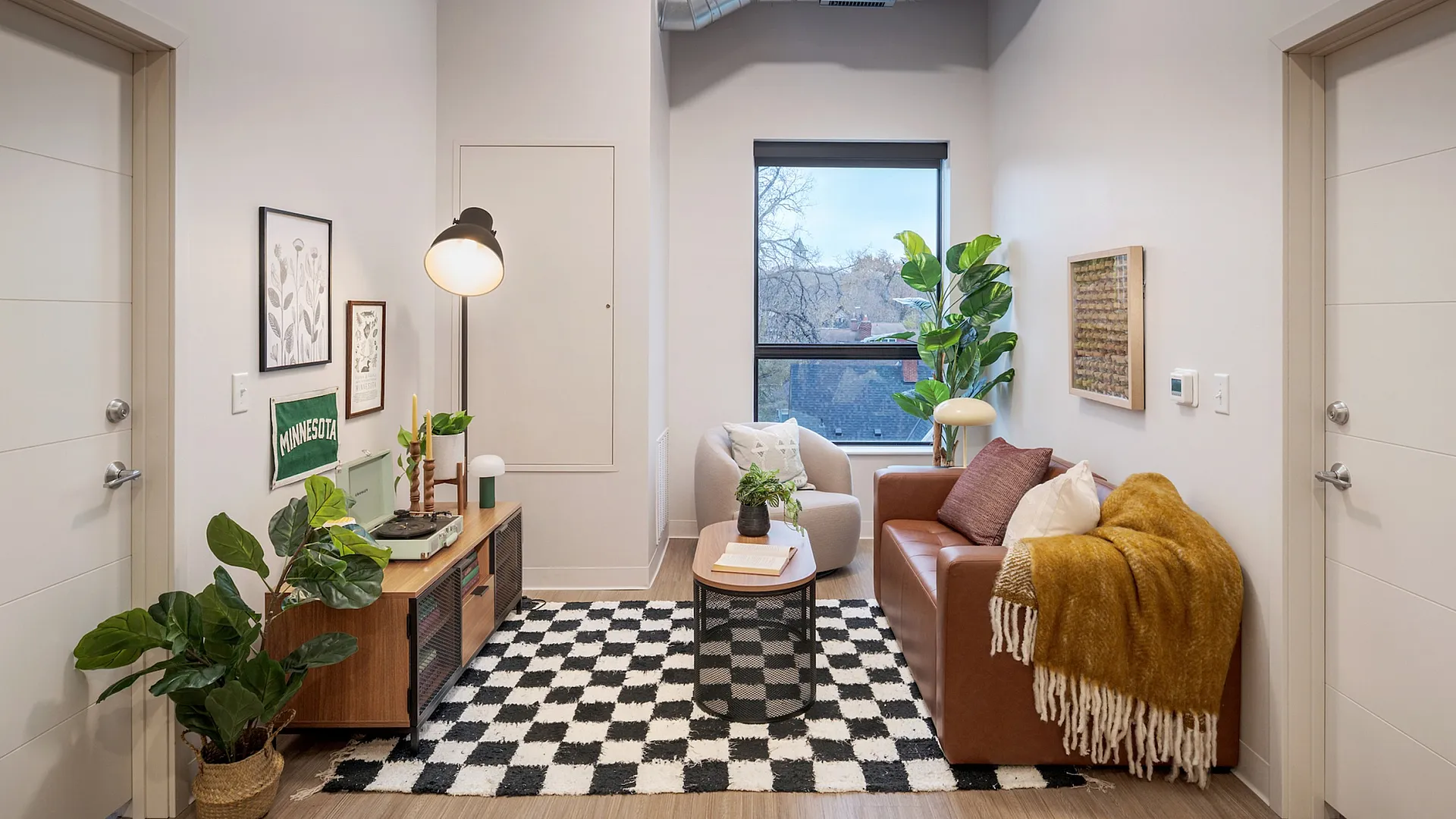 Chic urban living room featuring a stylish leather sofa, cozy seating area, modern decor, and large window with a view.