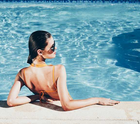 A woman in a yellow bikini is sitting by a pool.