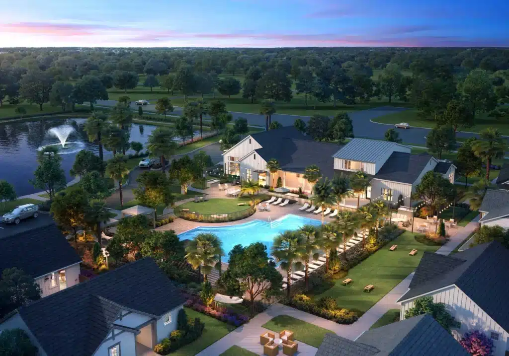 Aerial view of a residential community with a central swimming pool, lounge chairs, landscaped gardens, clubhouse, and nearby pond with a fountain at sunset.