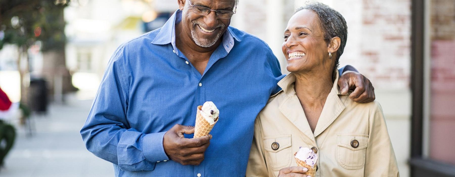 older couple walks down city sidewalk while holding ice cream cones