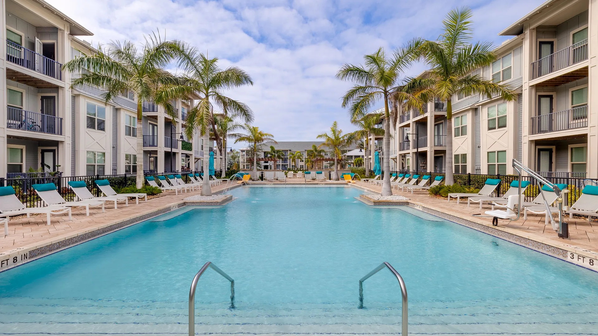 A serene pool area surrounded by palm trees and modern apartments.