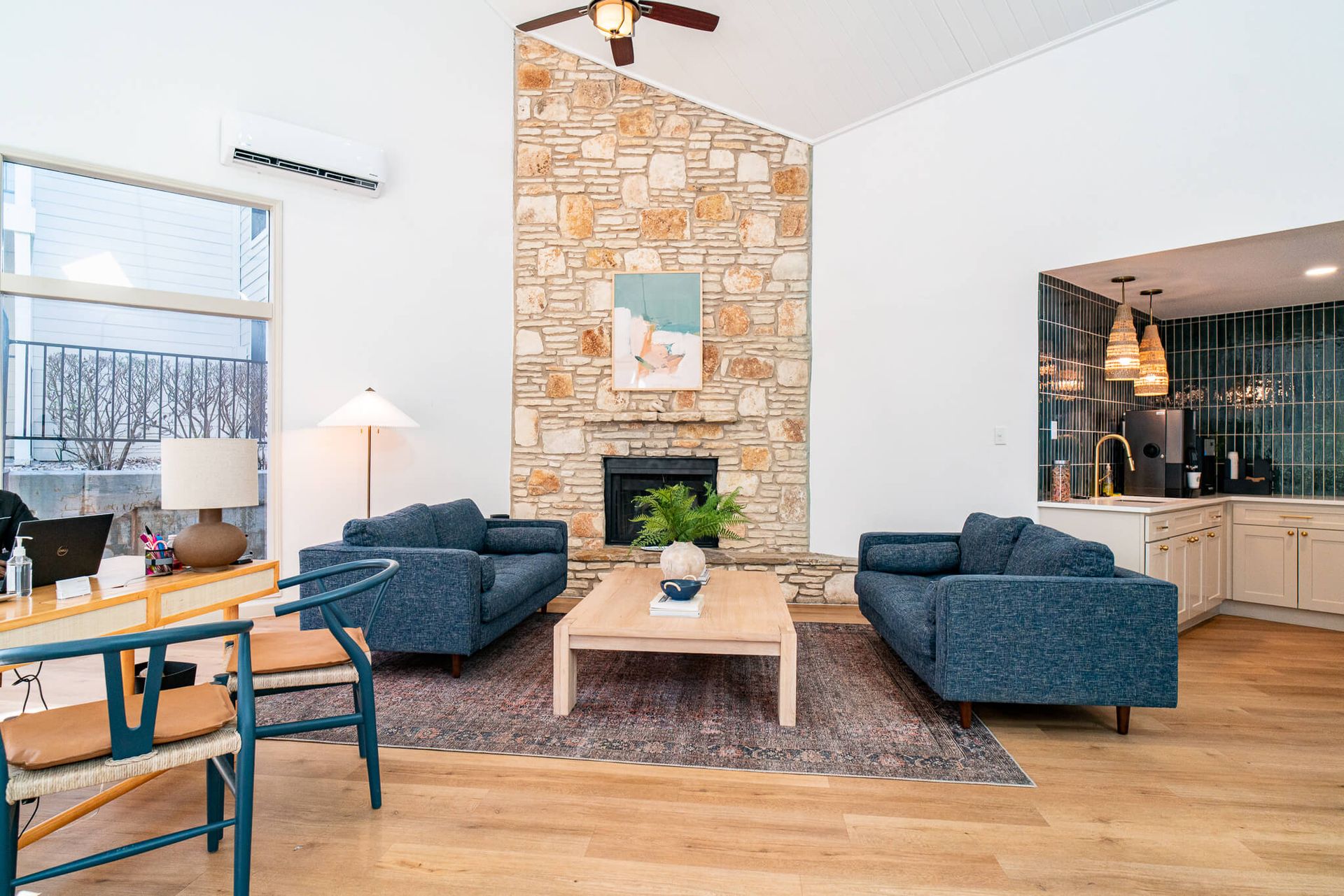 Spacious living room with a stone fireplace, two blue sofas, and an open kitchen in the background.