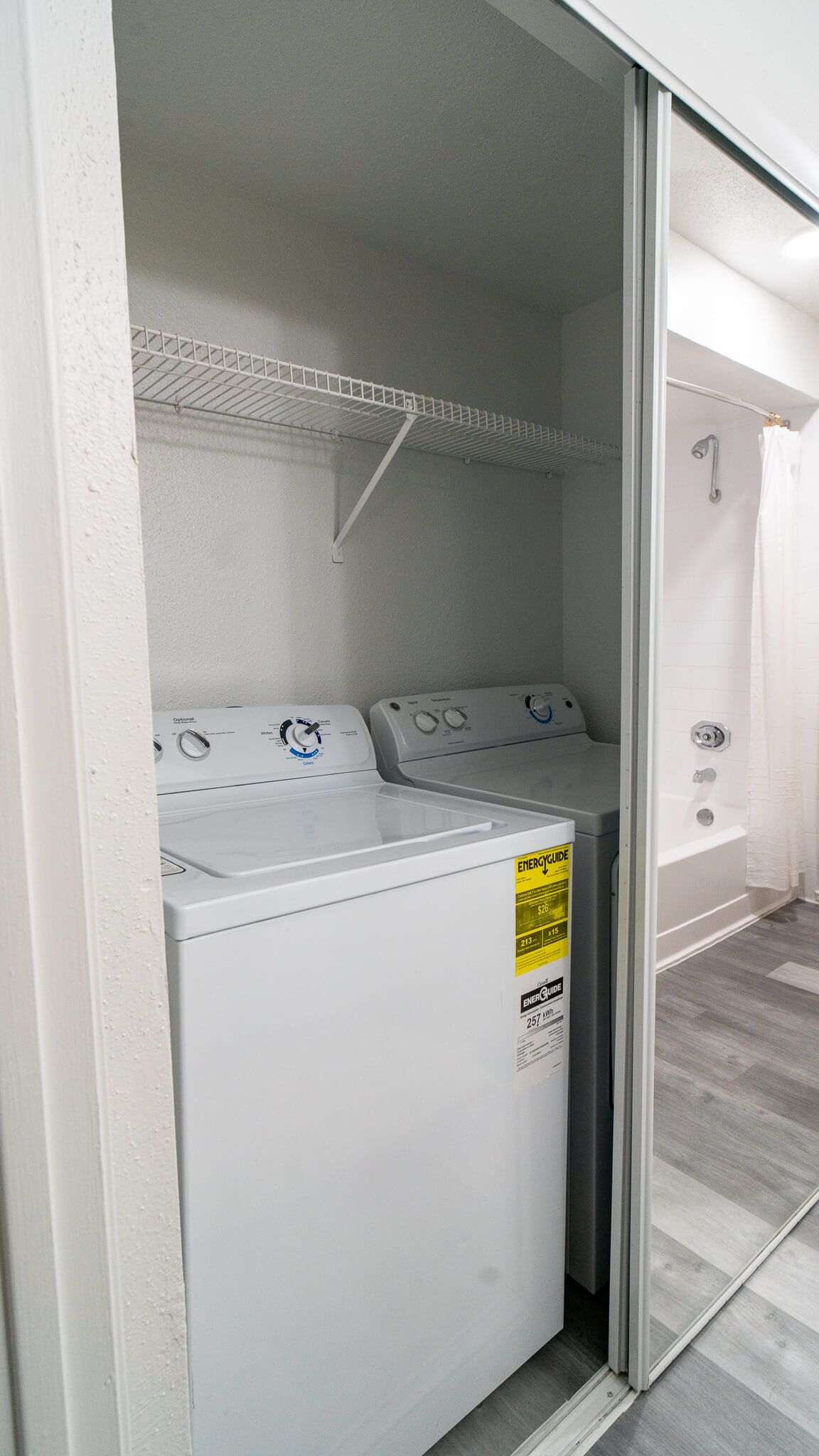 In-unit laundry closet with a white top-load washer and dryer and a wire shelf above.