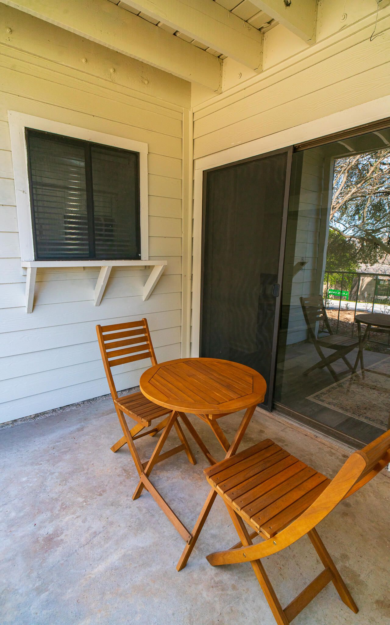 Patio balcony with a round wooden table and three folding chairs beside a sliding glass door.