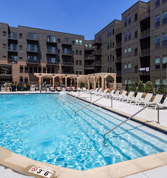 A swimming pool surrounded by apartment buildings and lounge chairs.