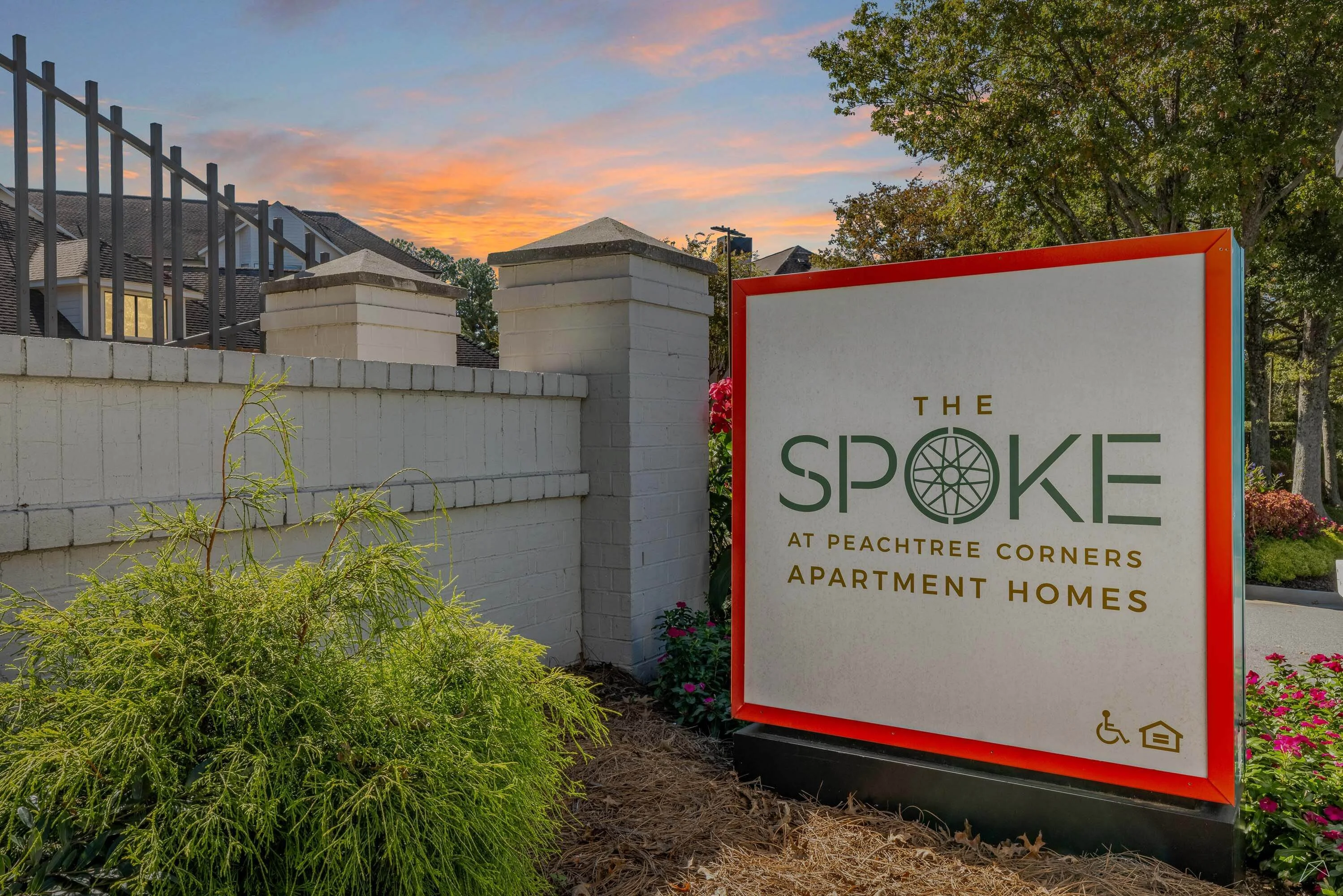 Welcome sign of The Spoke at Peachtree Corners Apartment Homes, framed by greenery and a sunset in the background.