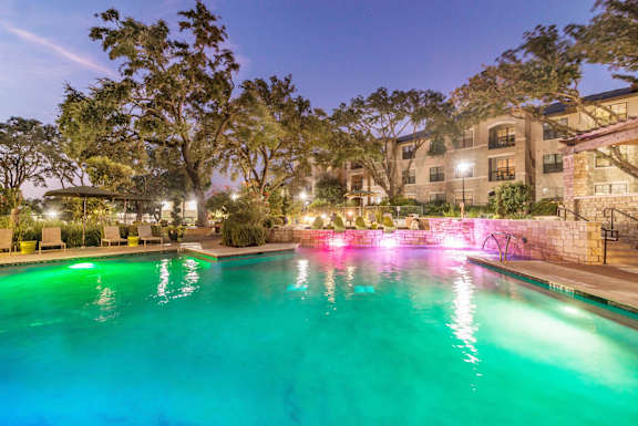 A pool lit up with green and pink lights at night.