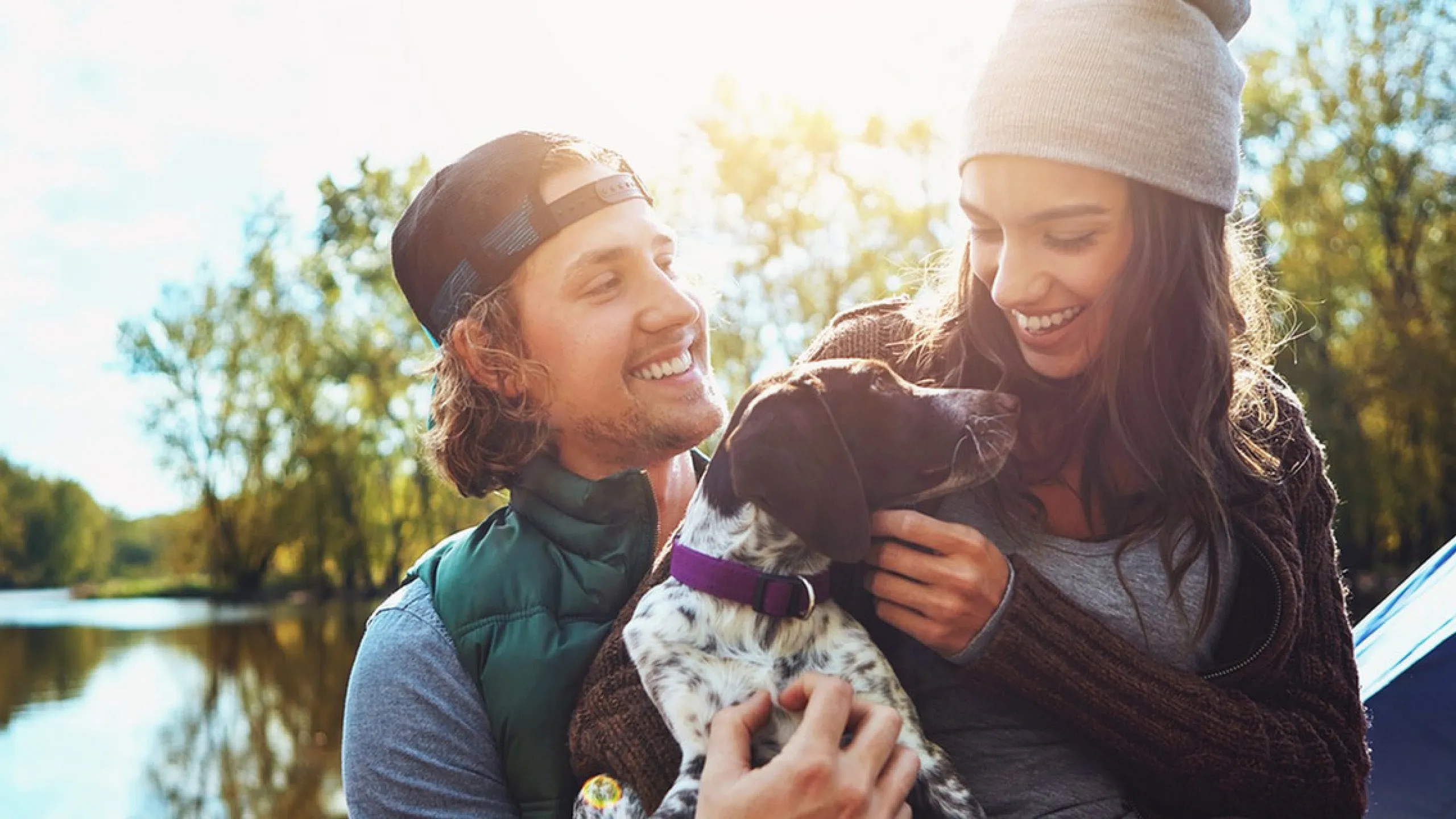 Happy couple enjoying a sunny day by the river with their dog.