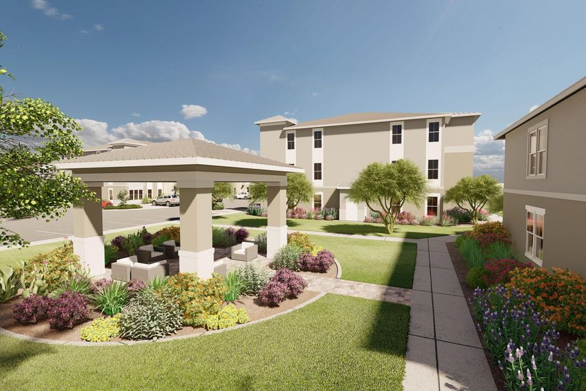 A landscaped outdoor area featuring a gazebo surrounded by colorful flower beds and greenery, leading to two multi-story buildings. The scene is bright and sunny with a blue sky and scattered clouds, creating a welcoming atmosphere for residents.
