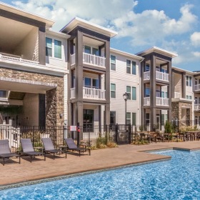 Resort-style pool with tanning shelf and lounge seating by apartment building