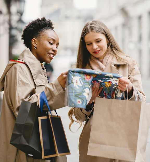 Two women holding shopping bags in front of a store window at Copper and Quarry Village, Maryland, 21209