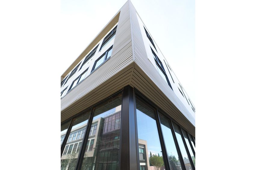 Modern building featuring a unique angular design with large glass windows and horizontal wooden paneling. The image captures the structure from a low angle, emphasizing its sleek lines and contemporary architecture set against a clear sky.