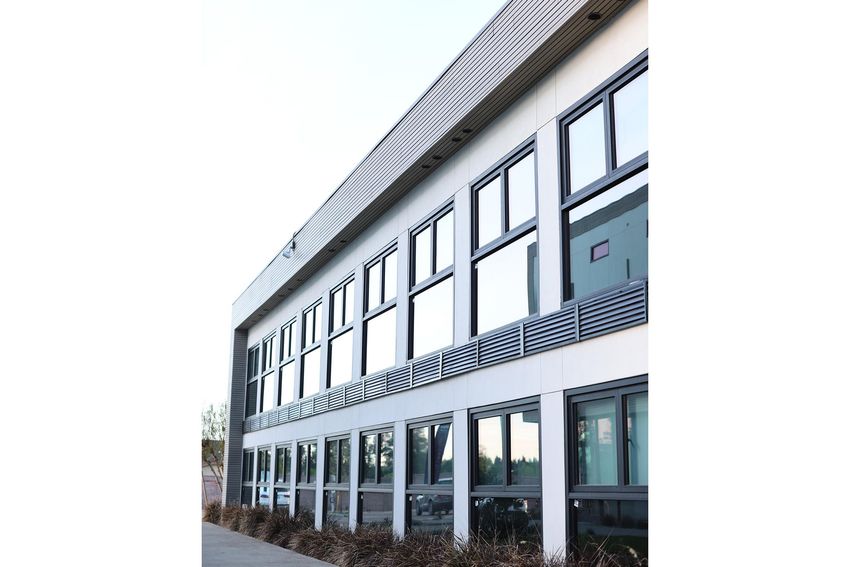 Modern building exterior featuring multiple large windows and a sleek design. The structure has a flat roof and is surrounded by sparse landscaping. The angle of the image shows the building's facade, emphasizing its clean lines and contemporary architecture.