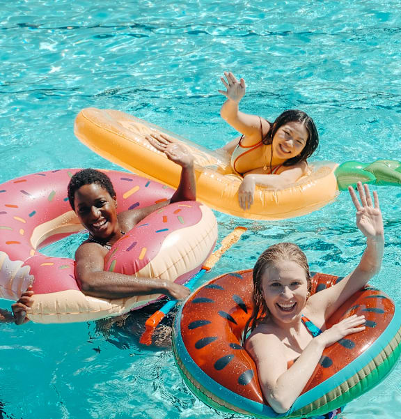 Three people are floating on colorful inner tubes in a pool.