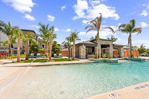 A swimming pool surrounded by palm trees and a house in the background at The Concord Luxury Apartments, Sarasota, FL