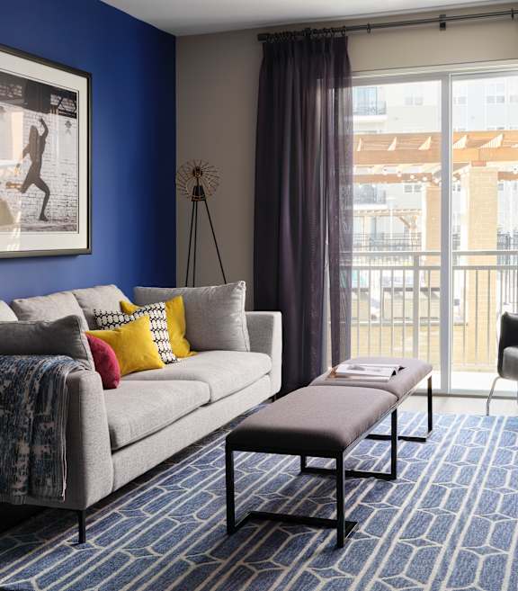 A living room with a grey sofa, a coffee table, and a large window with curtains.