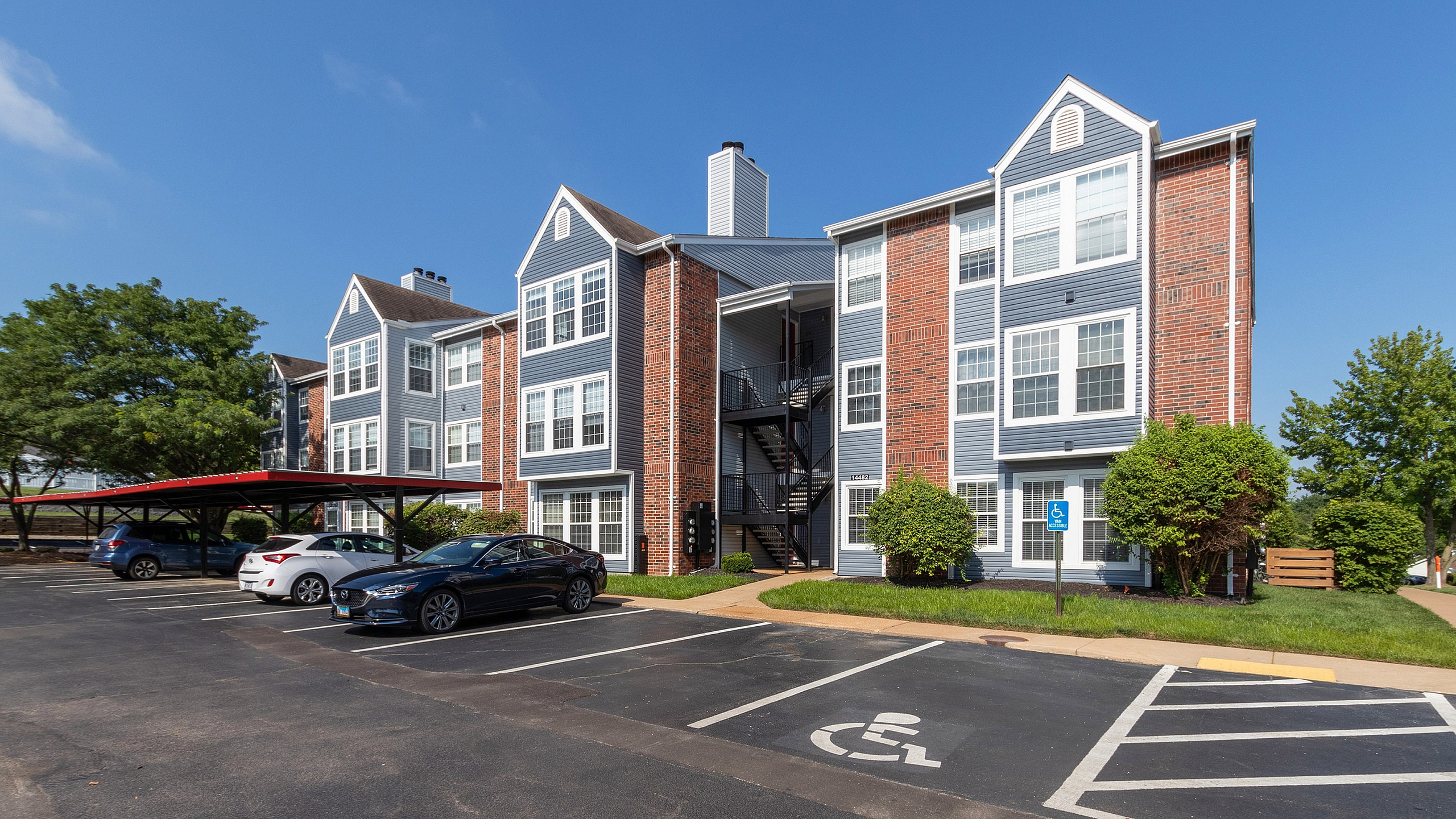 Charming three-story apartment complex with modern brick facade, surrounded by lush greenery and convenient covered parking.
