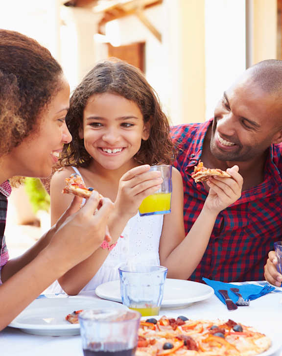 Four people eating pizza and drinking juice at a table.