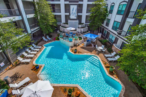 A swimming pool surrounded by lounge chairs and umbrellas in a courtyard. at Montecito Apartments, Houston, Texas