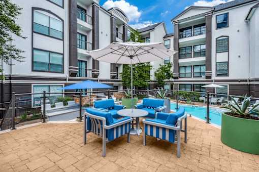 A patio with blue chairs and a white umbrella. at Montecito Apartments, Houston, TX